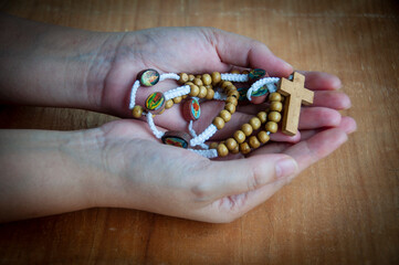 Hand holding Holy Rosary with wooden table background. Religious concept