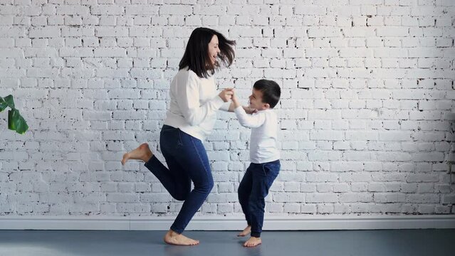 Active young mom babysiter and cute little kid son jumping dancing in modern house living room, happy family mother with child girl having fun enjoy playing funny activity together at home, 4k