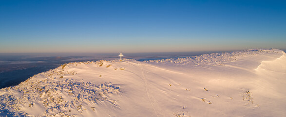 top view of the mountain top with a shining cross at sunrise in pink and purple tones. panorama of a mountain valley after a fresh snowfall.