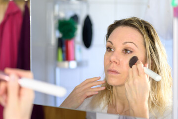 Woman applying highlight makeup on face.