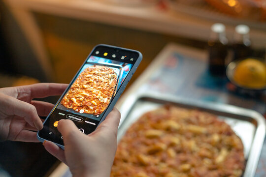 A woman takes a picture of a cooked pizza with a smartphone