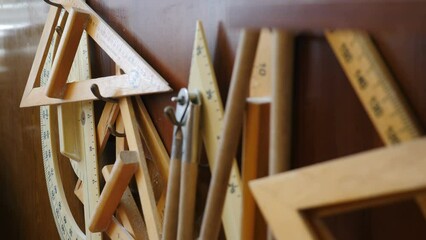 Set of big rulers for teachers. compasses and protractors hanging on classroom wall. Following focus. School blackboard kit for Maths or Geometry. Various tools for technical drawing in mess, 4 k - Powered by Adobe
