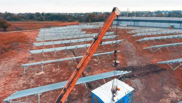 Construction site with installed metal constructions on the field. Male worker standing on top of the booth tries to attach machine hooks.