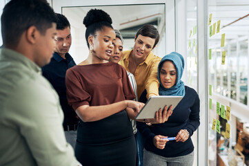 Obraz premium Technology helps them better understand their big plans. Shot of a group of businesspeople using a digital tablet while brainstorming with notes on a glass wall in an office.