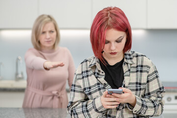 Angry woman scolds her teenage daughter, girl uses smartphone and ignores her mom. Family relationships
