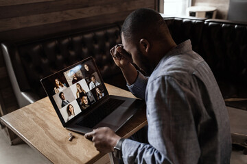 Exhausted tired African American businessman sitting at work desk with closed eyes, falling asleep, overworked young man, unmotivated student sleeping at workplace, boring routine work.