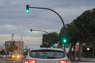 Traffic and cars on an urban avenue with green traffic lights at dusk.