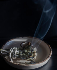 Smoke on dark background from burning sage incense, standing on a ceramic incense holder, selective focus