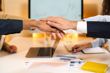 Close up view of the young creative multiracial team at the office gathered at the table, they bump their fists together. Teamwork of a multicultural group of people concept