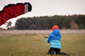 A cute child in a blue jacket and an orange hat sits on a green field, launches a parachute...
