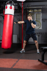 Young and strong mixed martial arts fighter practices punches with his right hand on punching bag in  gym. Preparation for competition.