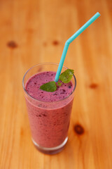 Top view on blackberry smoothie in glass cup with mint sheets and tube on wooden table