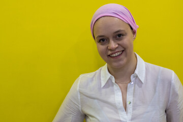 Close-up of a young smiling woman wearing a pink scarf in reference to cancer on yellow background