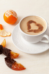 Cup of delicious morning coffee with cinnamon heart, whole orange and orange slice in chocolate
