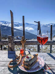 Cake, Aperol Spritz and schnapps made from the bark of the pine tree on the summit of the Patscherkofel with a view over the snowy peaks of the Tux Alps around Tyrol's provincial capital Innsbruck - obrazy, fototapety, plakaty
