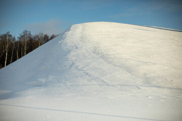 Fototapeta premium Mountain of snow. Snowy slope. Winter day. Sun is shining on hill. Natural object in park.