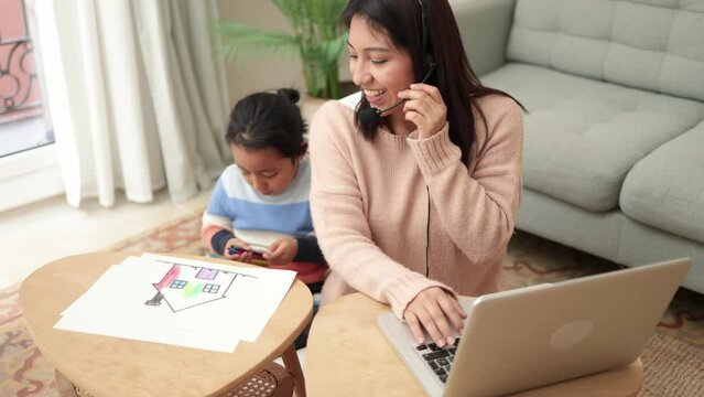 Happy asian mother working on computer at home with her child - Busy family mom giving call center support