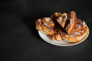 Beautiful serving and serving of cinnabon. Sliced cinnabons on a white plate stand on a black table.