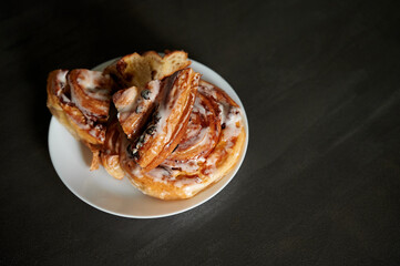 Beautiful serving and serving of cinnabon. Sliced cinnabons on a white plate stand on a black table.