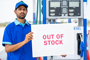 Worker at petrol or gas filling sation showing out of stock notice sign board - concept of economy...