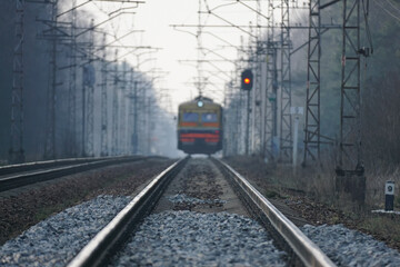 Fototapeta na wymiar Train rides on rails, red traffic light, evening foggy time