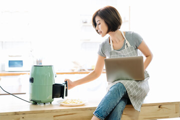 Busy beautiful Asian woman work from home using laptop computer while taking tasty french fries...