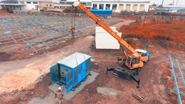 Location prepared for installing solar panels. Workers go around equipment booth just set with crane. Top view.