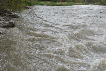 murky, rapidly flowing river water and river bank