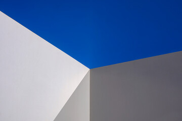 Sunlight and shadow on surface of white cement wall in perspective view against blue clear sky,...