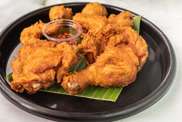 Appetizing fried chicken that sits on a banana leaf in a black plate.