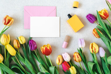 Colorful spring mockup of bright tulips, perfume, and card on a neutral background.