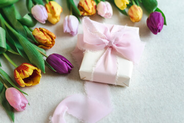 Layout of a beautifully wrapped gift decorated with a silk ribbon and surrounded by spring tulips.