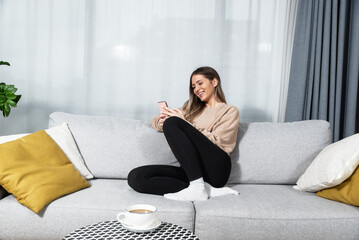 Smiling teenager girl relax lying on sofa at home using cellphone texting chatting with friend, happy young woman on couch hold smartphone shop online or check mobile application or social media