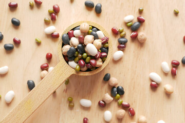 close up of mixed beans in a wooden spoon on table 