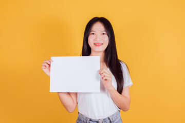 Beautiful woman with long dark hair wears white t-shirt holding empty white paper and space for text on yellow background