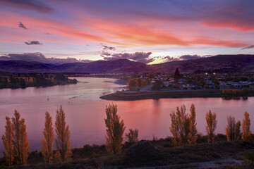 Naklejka na ściany i meble The town of Cromwell in the South Island of New Zealand, at sunset. The colorful clouds are reflected in the waters of Lake Dunstan