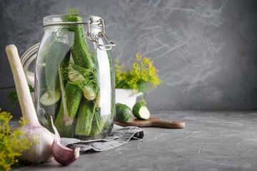 Pickling and fermentation cucumber in glass jar with dill and garlic on dark grey concrete tabletop. Space for text and design.