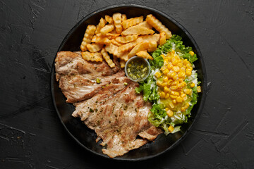 carne de cerdo a la plancha con lechuga y papas fritas sobre un fondo negro