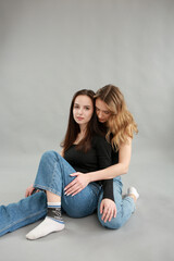 stylish photo shoot of two models blonde and brunette on a gray background in jeans and a black T-shirt. two girlfriends hugging. posing during a photo shoot. young beautiful girls lookbook model