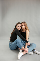 stylish photo shoot of two models blonde and brunette on a gray background in jeans and a black T-shirt. two girlfriends hugging. posing during a photo shoot. young beautiful girls lookbook model