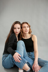 stylish photo shoot of two models blonde and brunette on a gray background in jeans and a black T-shirt. two girlfriends hugging. posing during a photo shoot. young beautiful girls lookbook model