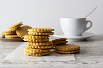 Cookies with cream filling lie in a stack on white parchment. A white cup of coffee in the background. Light background
