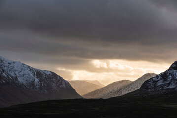 Majestic dramatic Winter sunset sunbeams over landscape of Lost Valley in Etive Mor in Scottish Highlands