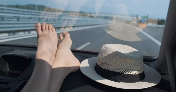 Close-up, woman legs on inside driving car, on sunny highway. Traveling by car in summer. Point of view 4k footage. Copy space for text. Auto traveling, lifestyle. Road trip. Girl enjoying car travel