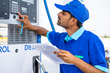 Petrol pump worker noting or writing fule meter at petroleum station - concept of employment, jobs and gas filling station.