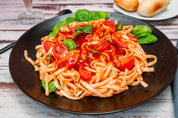 Spaghetti pasta with an exquisite tomato sauce with homemade basil leaves served on a black plate on a rustic table. Close up. High view.