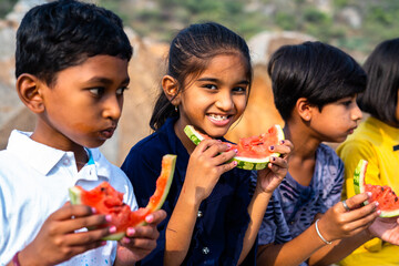 girl kid looking camera while group of kids busy eating watermelon during hot summer day - concept...