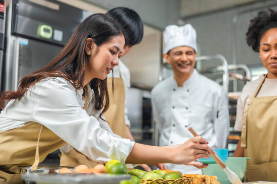 Cooking  course , senior Asian male chef in cook uniform teaches young asian and african american people cooking class students to prepare, mix ingredients for pastry foods, in restaurant stainless 