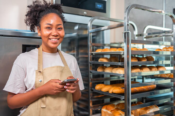 Close up of joyful African American young woman worker in apron stands in bakery shop, speking on...