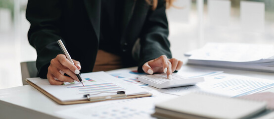 Close up of businesswoman or accountant hand holding pen working on calculator to calculate business data, accountancy document and laptop computer at office, business concept